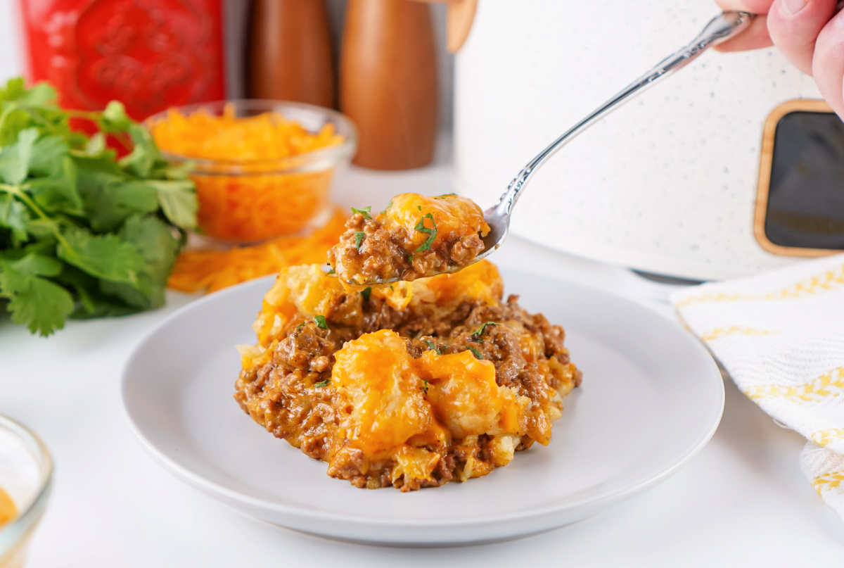 Close-up of a bite of taco tater tot casserole with melted cheese and seasoned ground beef.