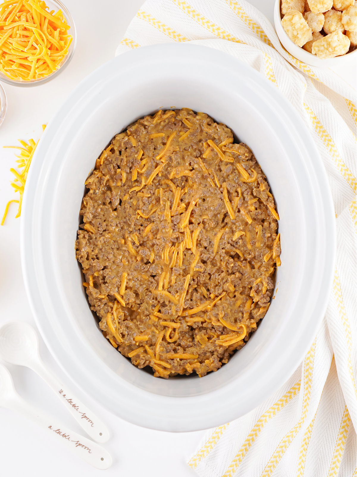 Seasoned ground beef and cheese sauce mixture spread evenly over tater tots in a crockpot.