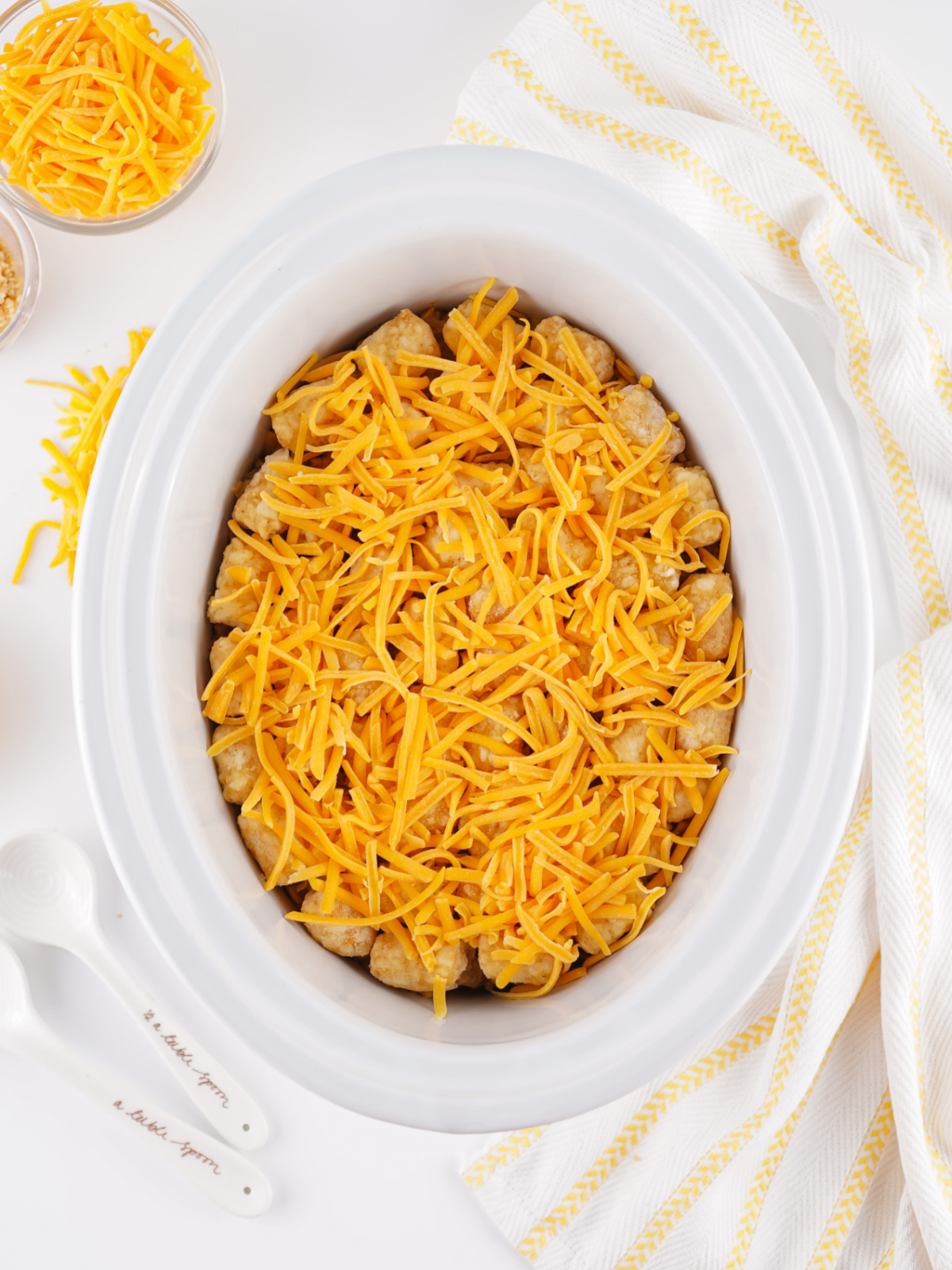 Frozen tater tots and shredded cheddar cheese layered on top of taco casserole in a crockpot.