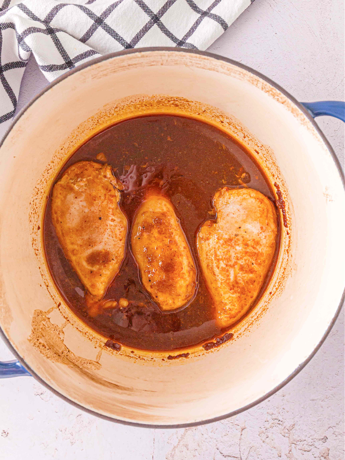 Three chicken breasts simmering in a rich BBQ-style sauce inside a Dutch oven.