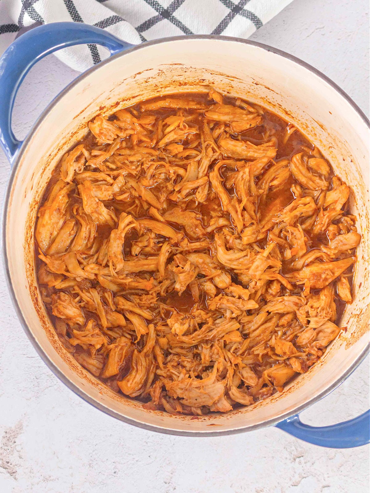 Fully cooked BBQ chicken shredded and mixed into sauce inside a Dutch oven.