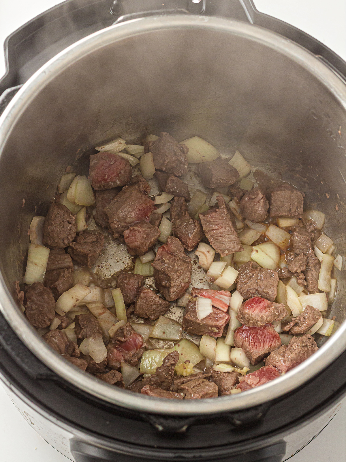 Beef stew meat browning with chopped onions and garlic in the Instant Pot using the sauté function.