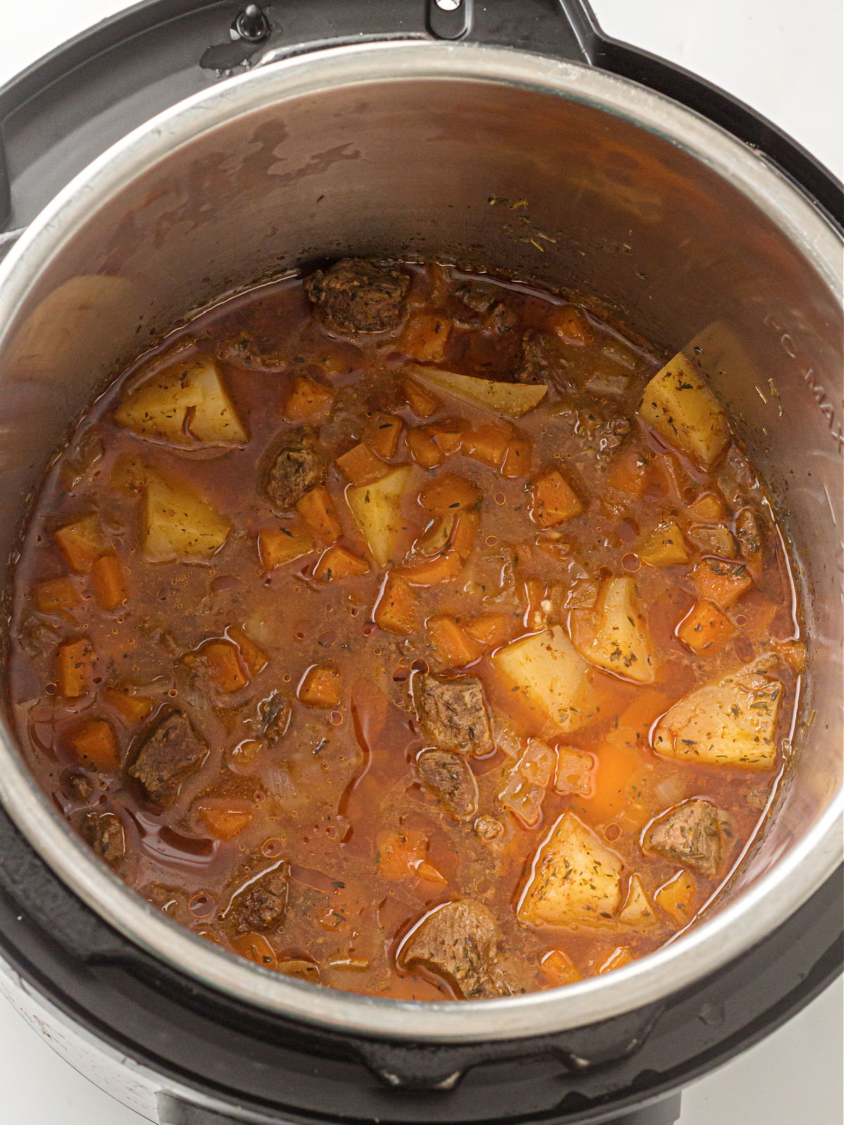 Beef stew cooking inside the Instant Pot, showing beef chunks, carrots, potatoes, and seasoned broth after pressure cooking.
