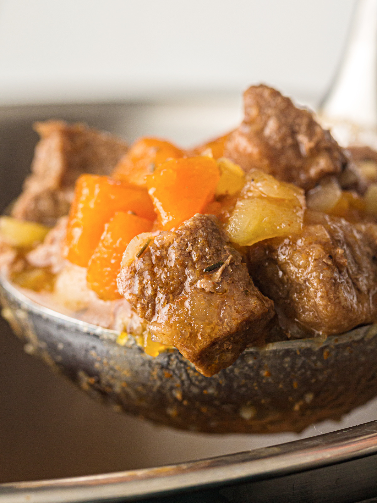 Close-up of a spoon lifting tender beef stew with carrots and potatoes from the pot.
