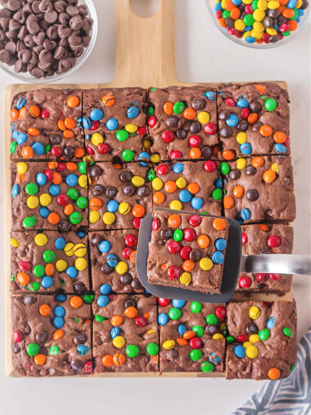 Sliced M&M brownies arranged in a grid, with one brownie square lifted on a spatula.