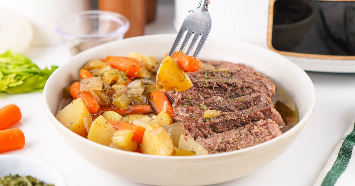 Close-up of slow cooker seasoned chuck roast with tender potatoes, carrots, celery, and onions in a savory broth.
