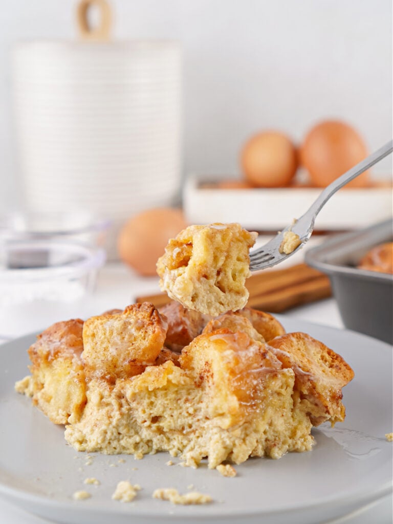 A fork lifting a bite of donut bread pudding from a plate, showing the soft custardy texture and lightly glazed donut pieces.