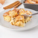 A fork lifting a soft bite of donut bread pudding showing the custardy interior and lightly glazed top.
