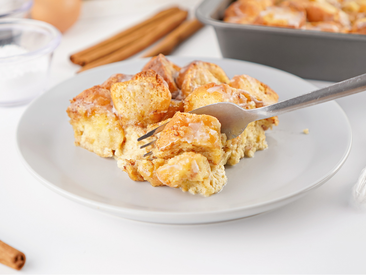 A fork lifting a soft bite of donut bread pudding showing the custardy interior and lightly glazed top.