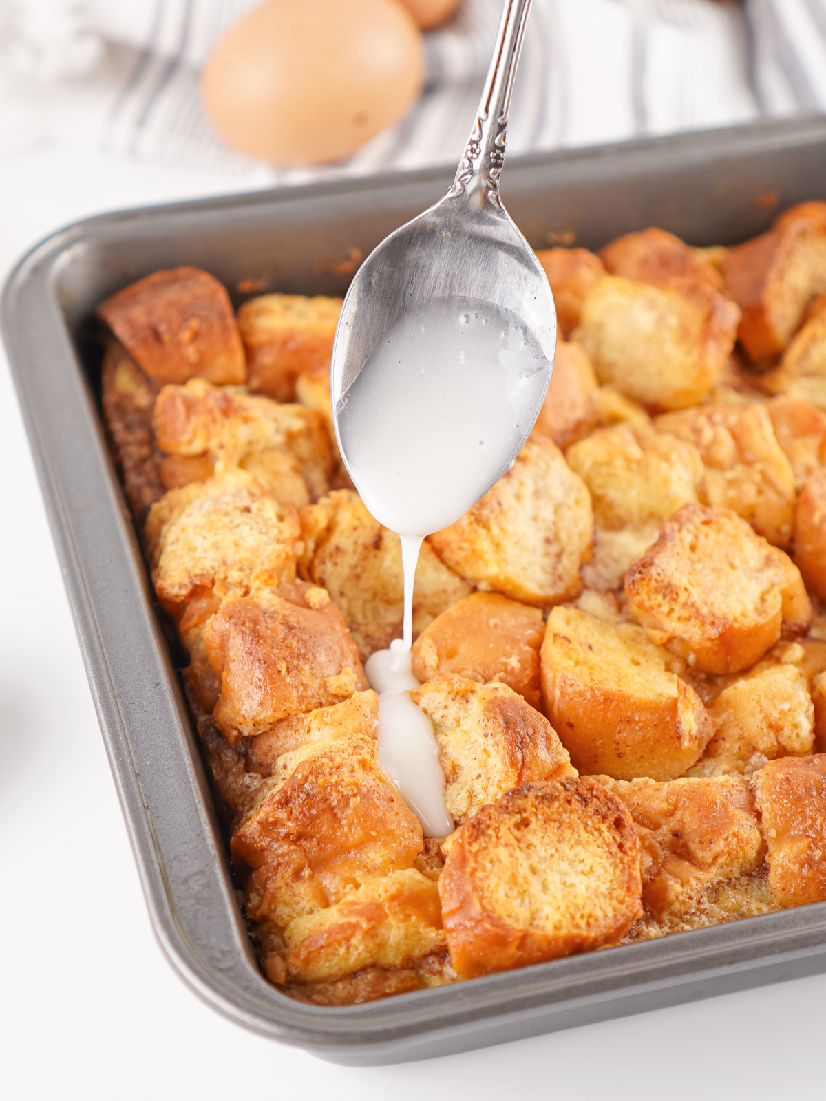 Vanilla glaze spooned over warm donut bread pudding fresh from the oven.