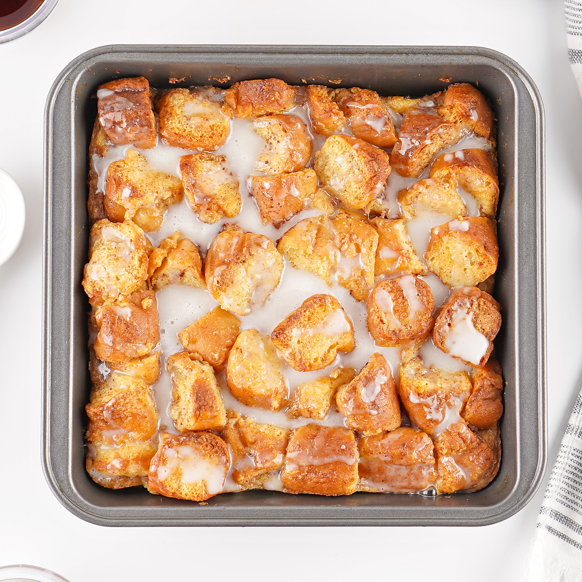 Leftover donut bread pudding baked until golden and drizzled with vanilla glaze in a square baking pan.