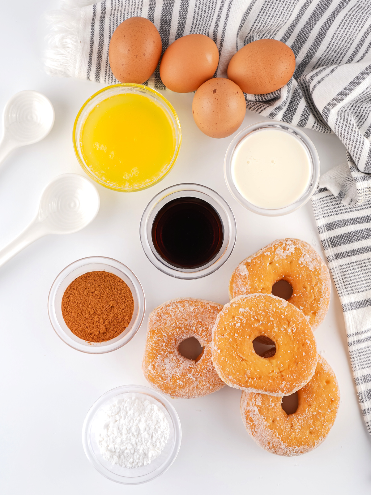Ingredients for donut bread pudding including glazed donuts, eggs, melted butter, cinnamon, milk, vanilla, and powdered sugar.