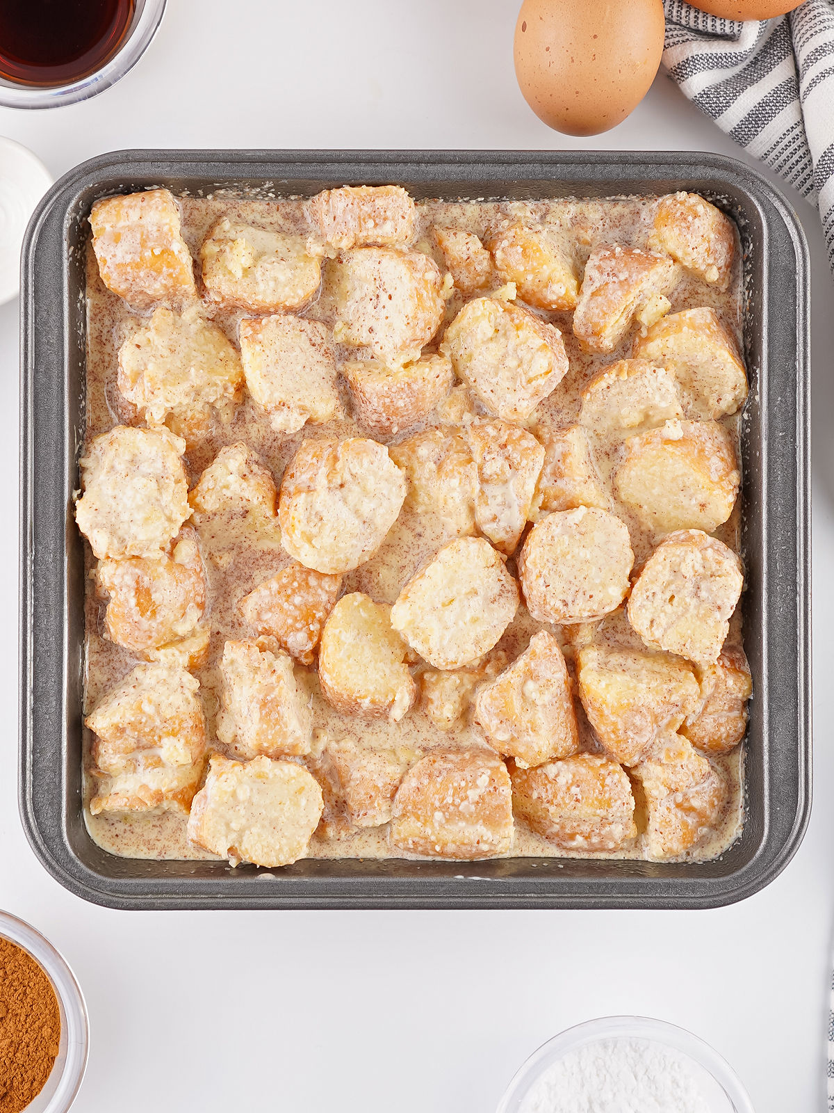 Unbaked donut bread pudding mixture spread evenly in a square baking pan.
