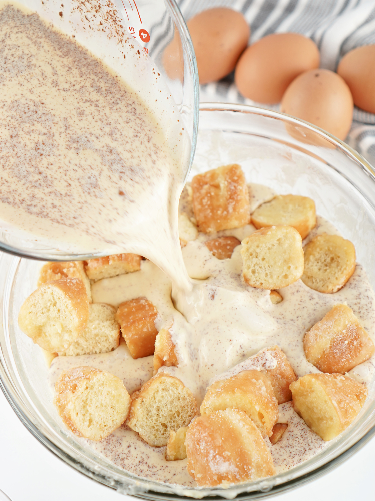 Cinnamon custard being poured over donut pieces to fully saturate the bread pudding.