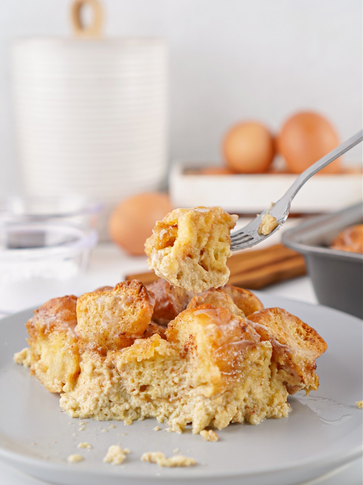 A fork lifting a bite of donut bread pudding from a plate, showing the soft custardy texture and lightly glazed donut pieces.