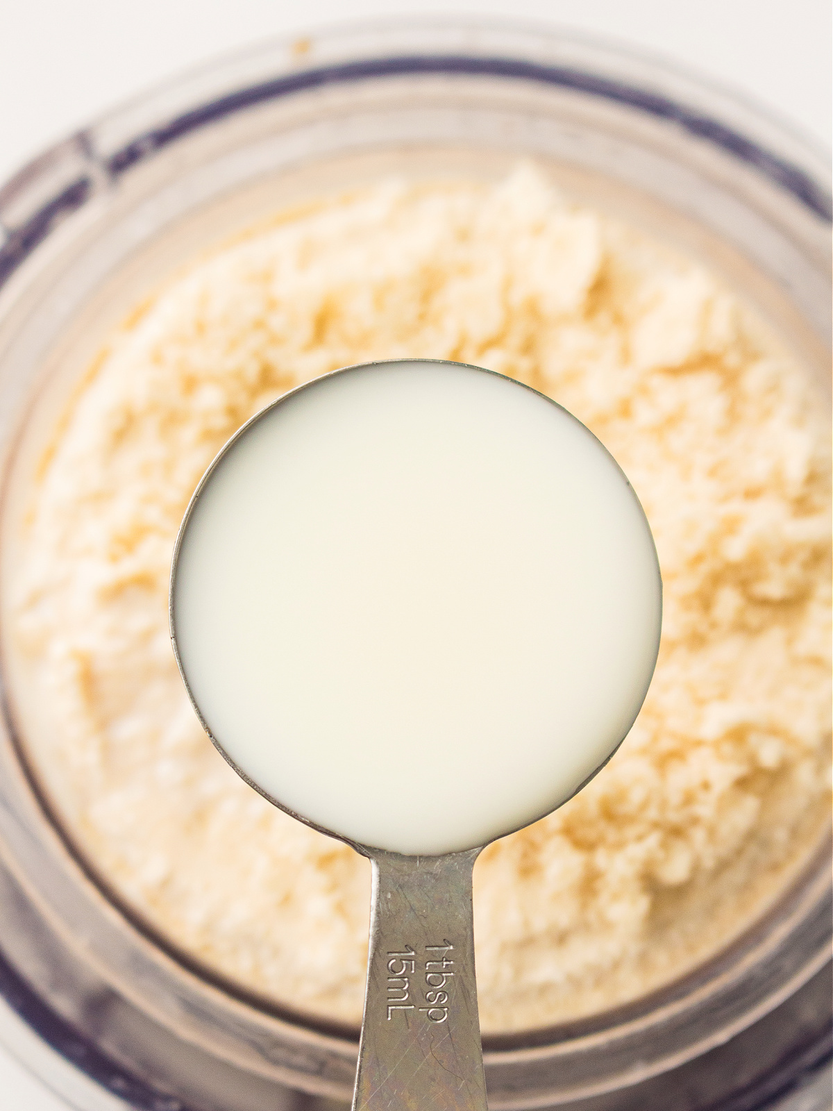 Measuring spoon filled with milk held over blended high protein ice cream base.
