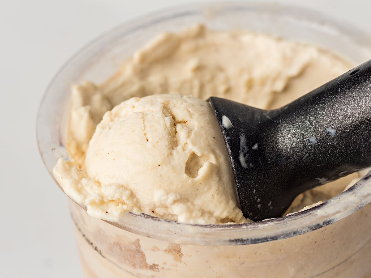 Black ice cream scoop resting in a Ninja Creami container filled with protein ice cream.