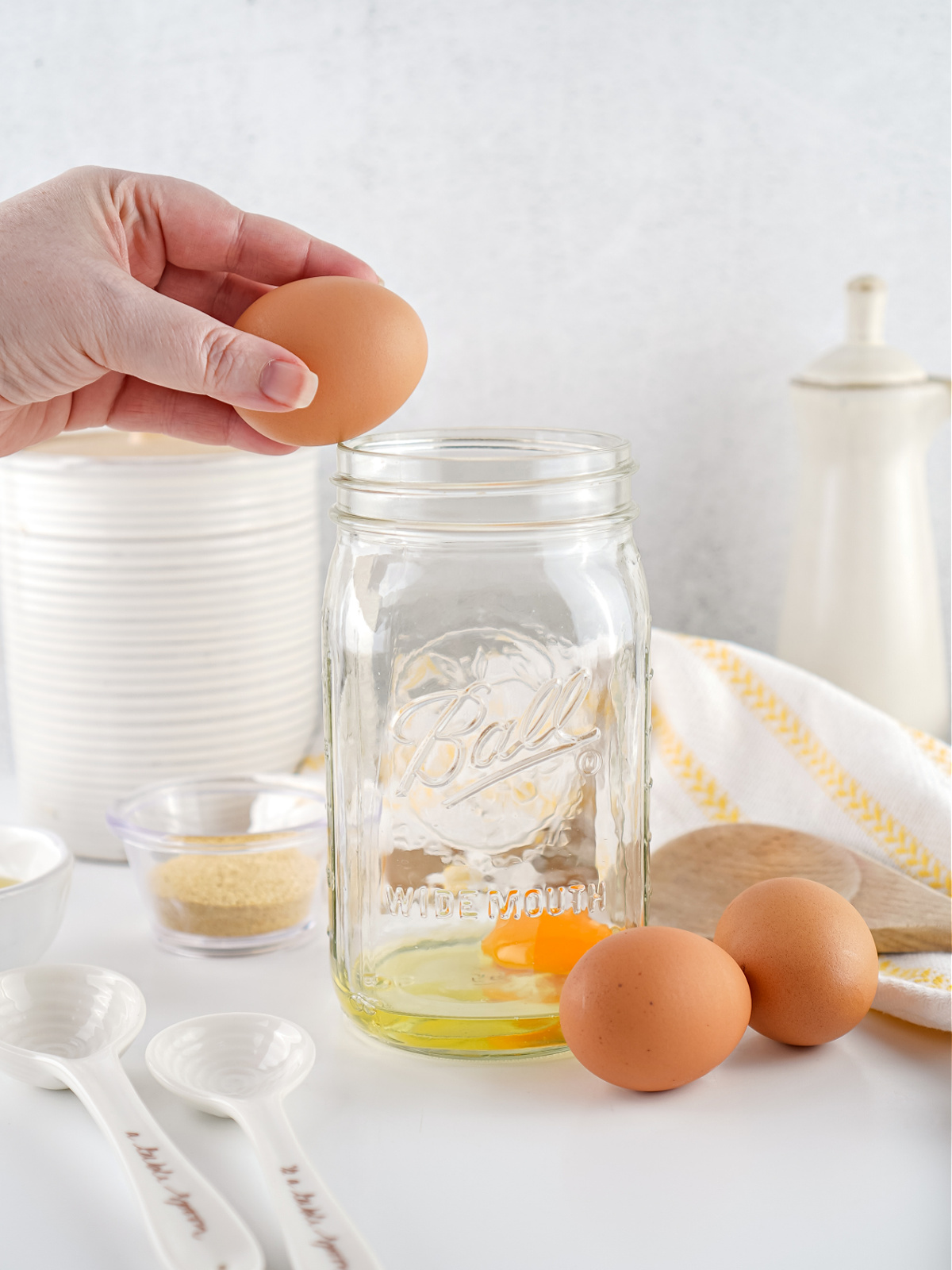 Hand adding a raw egg to a mason jar for homemade mayonnaise.