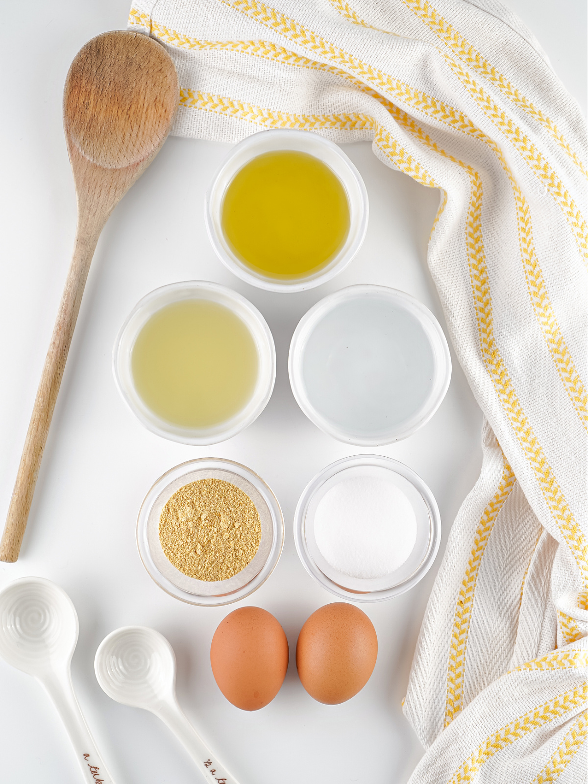 Homemade mayonnaise ingredients arranged on a white surface with eggs, oil, vinegar, lemon juice, salt, and mustard.