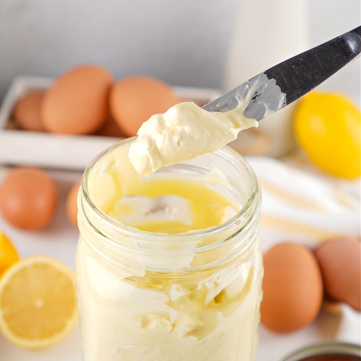 Knife lifting a dollop of finished homemade mayonnaise from a jar.