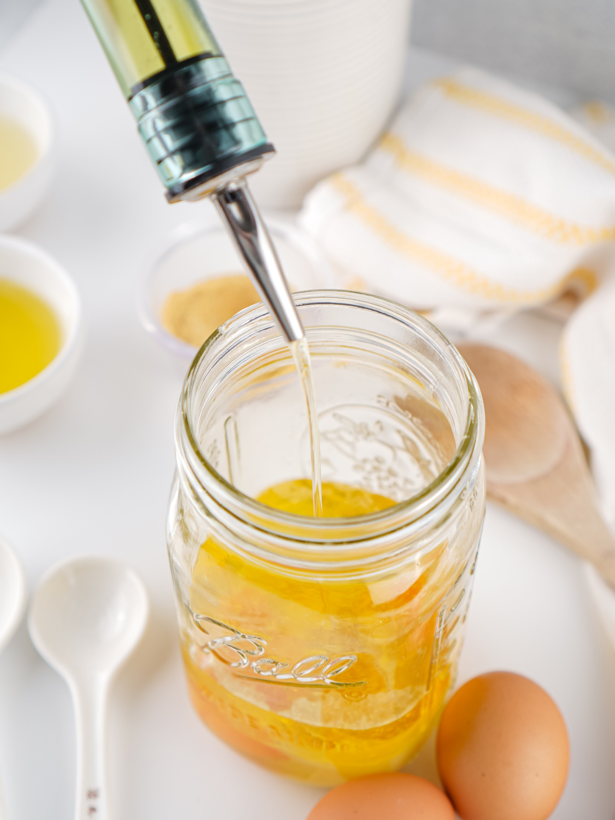 Olive oil being poured into a mason jar with eggs for mayonnaise.