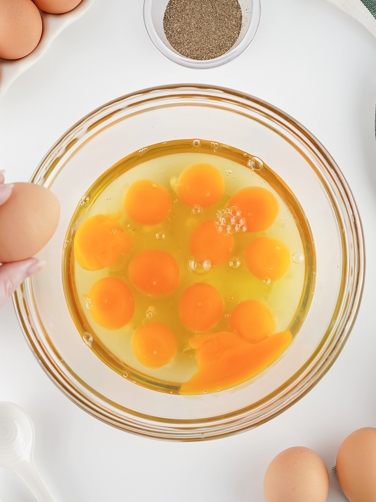 Overhead view of raw eggs cracked into a glass bowl, ready to be seasoned and whisked.