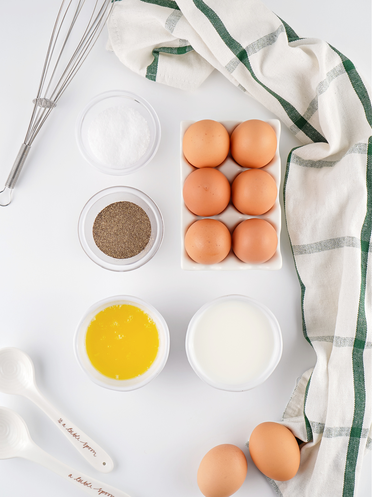 Ingredients for crockpot scrambled eggs arranged on a white surface, including eggs, milk, butter, salt, and pepper.