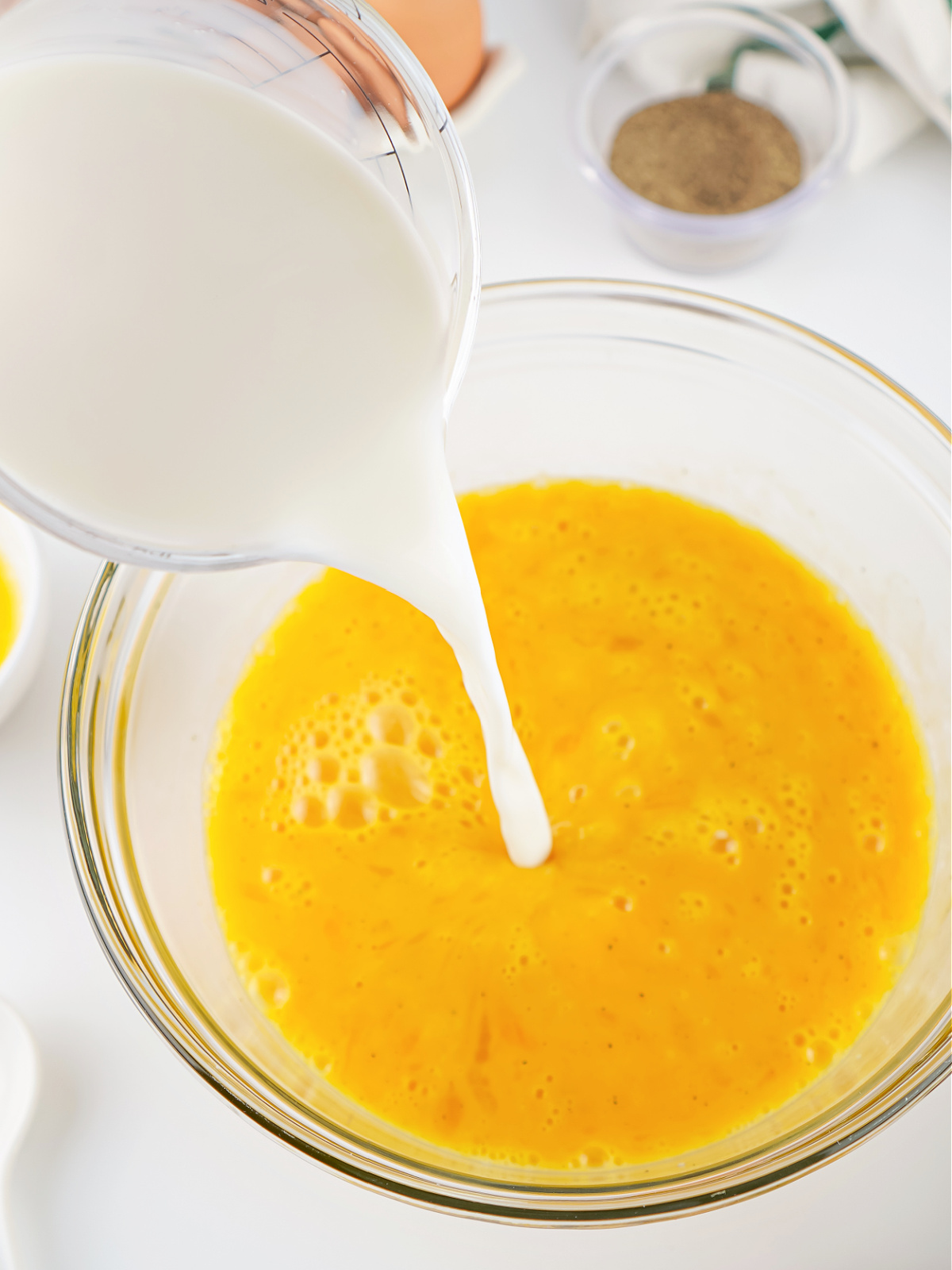 Milk being poured into a bowl of beaten eggs to create a creamy scrambled egg mixture.