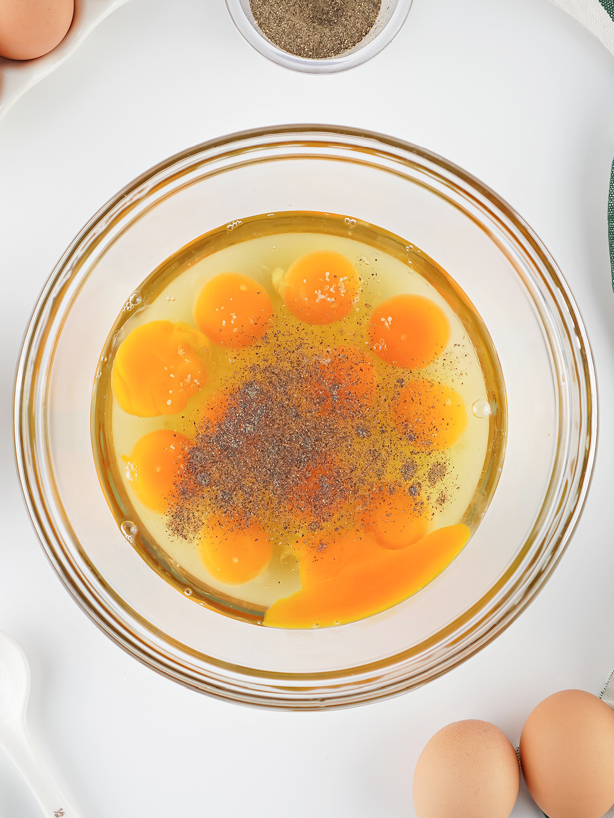 Raw eggs cracked into a glass bowl with salt and pepper sprinkled on top before mixing.