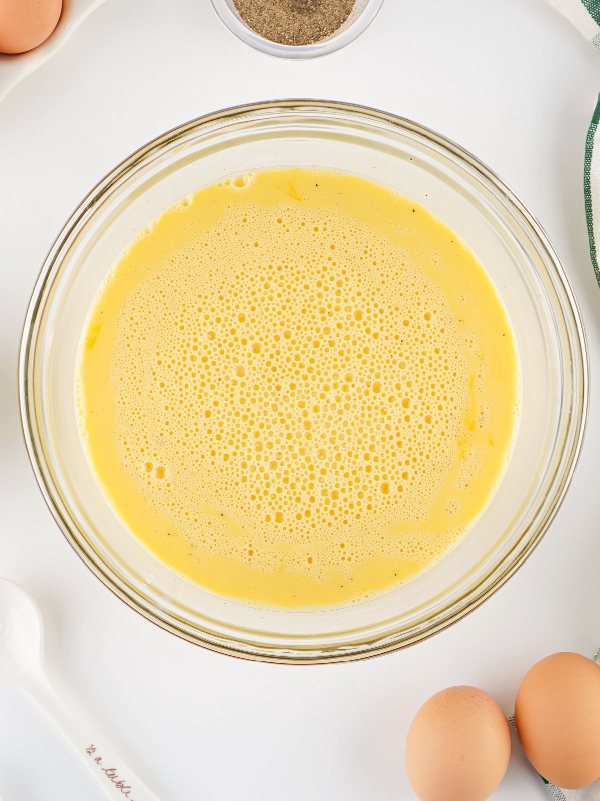 Overhead view of whisked eggs in a clear glass bowl, lightly foamy and ready for cooking.