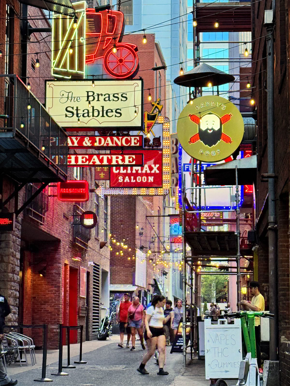 Neon signs and string lights illuminate a lively downtown Nashville alley lined with bars and restaurants.