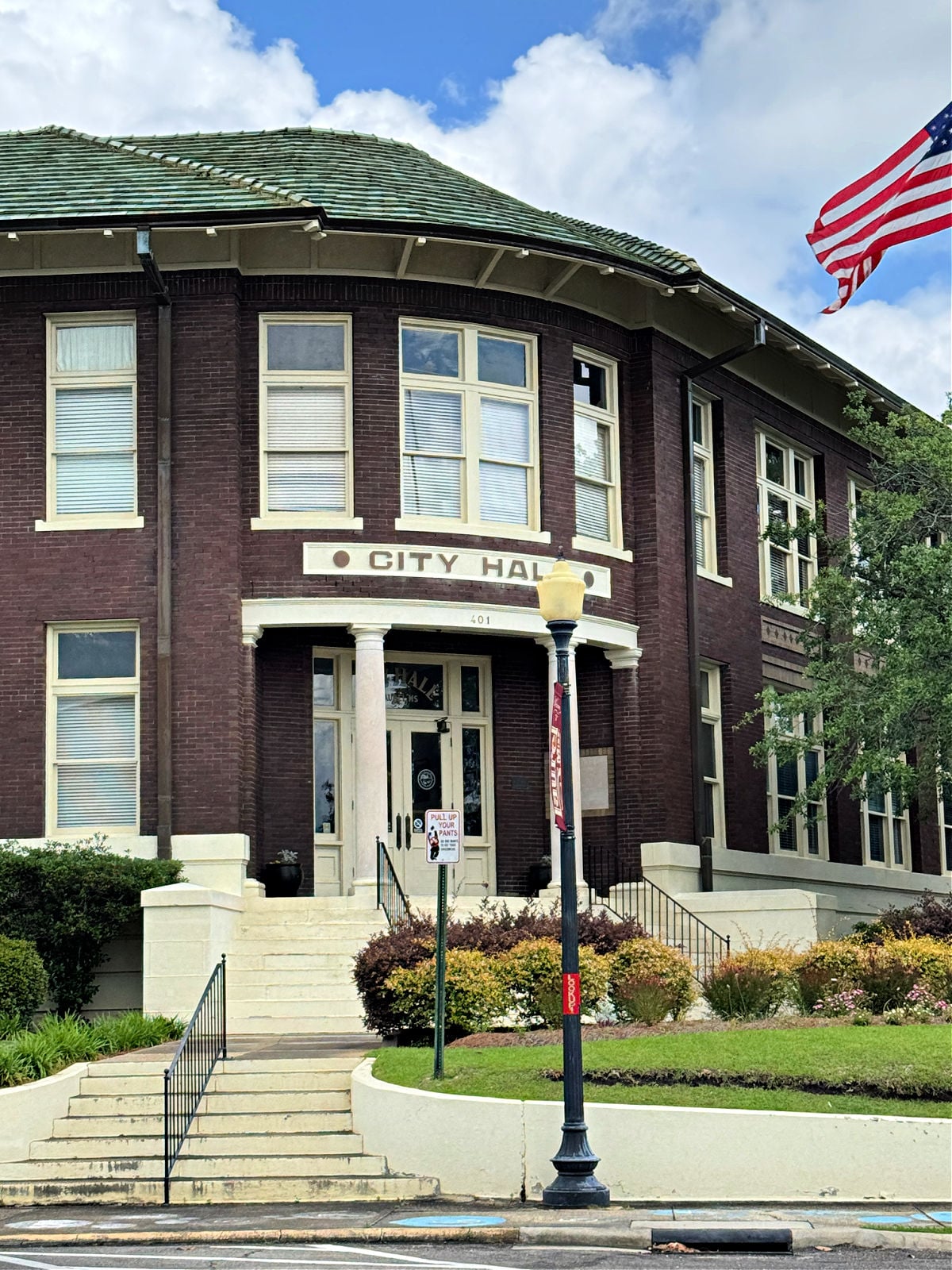 Historic brick Laurel City Hall building with white columns, landscaped steps, and an American flag flying overhead.