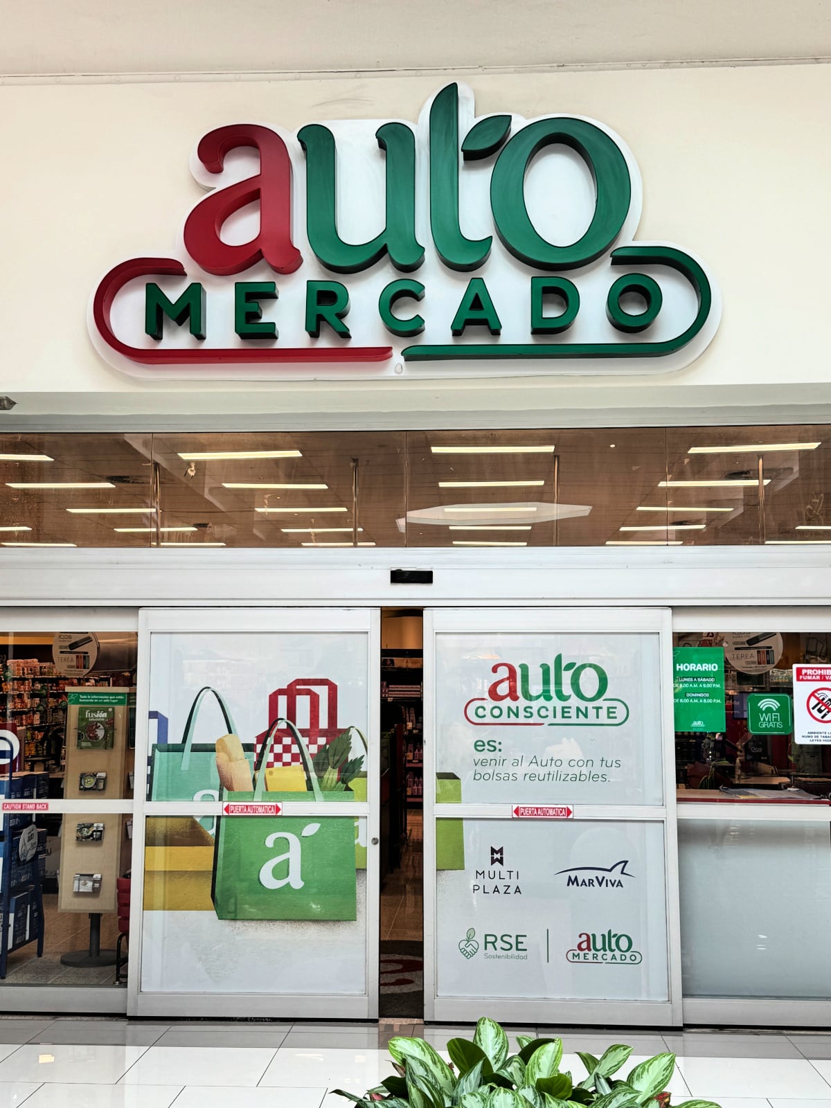 Entrance to Auto Mercado grocery store in Costa Rica with sliding glass doors and green and red signage.