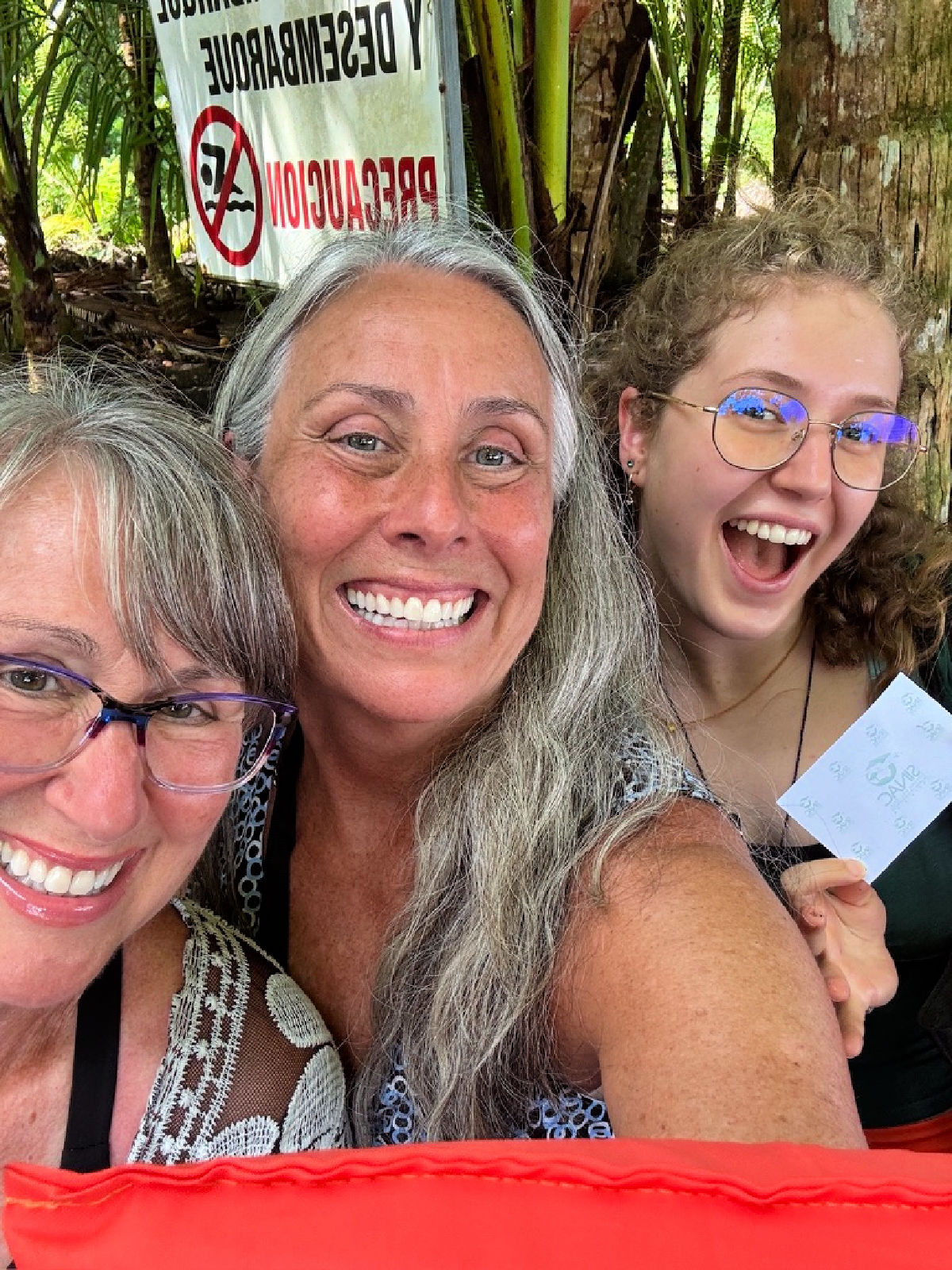 Three smiling women posing for a selfie outdoors in Costa Rica with tropical foliage behind them.