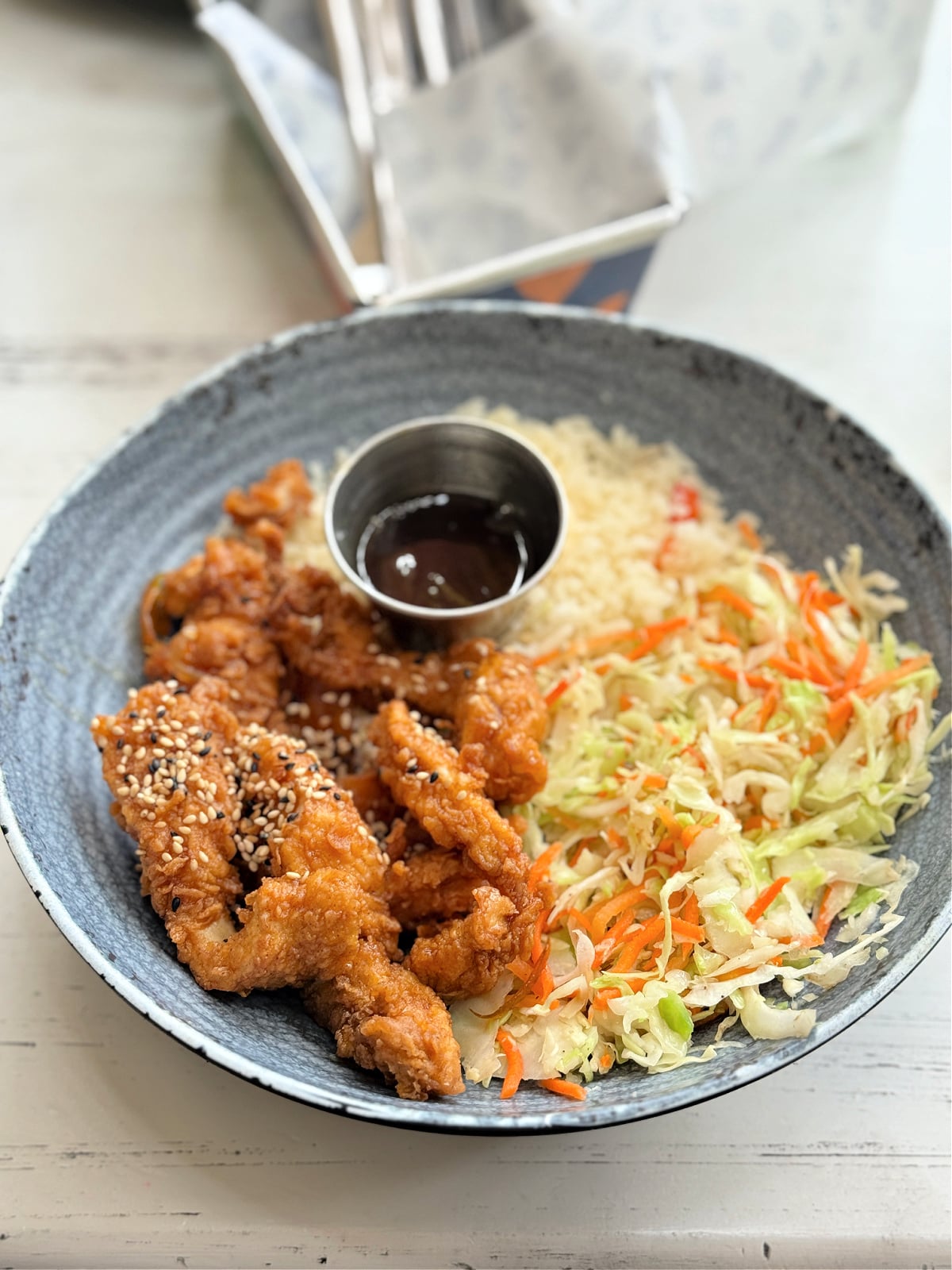 Bowl of crispy fried chicken with sesame seeds, rice, and coleslaw served in Costa Rica.