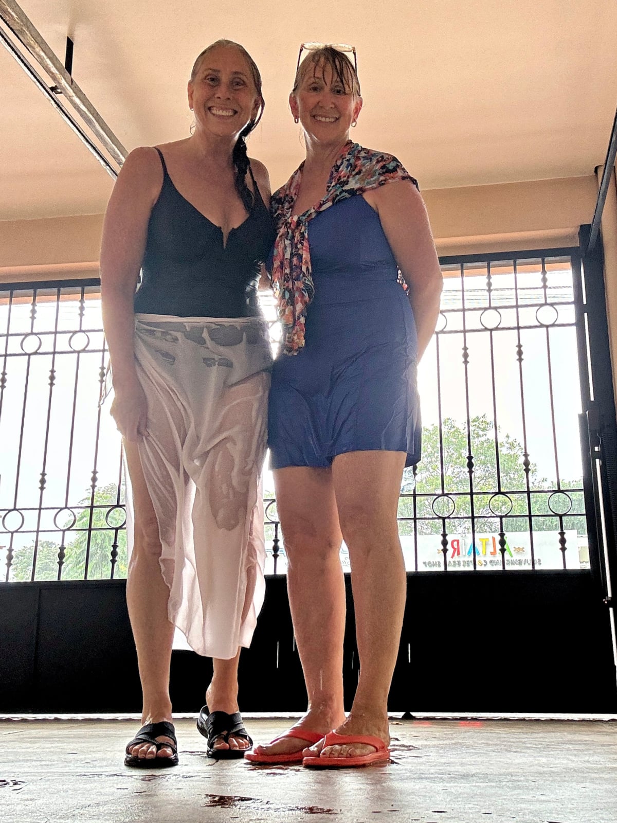 Two women standing indoors during a rain shower in Costa Rica with bright daylight behind them.