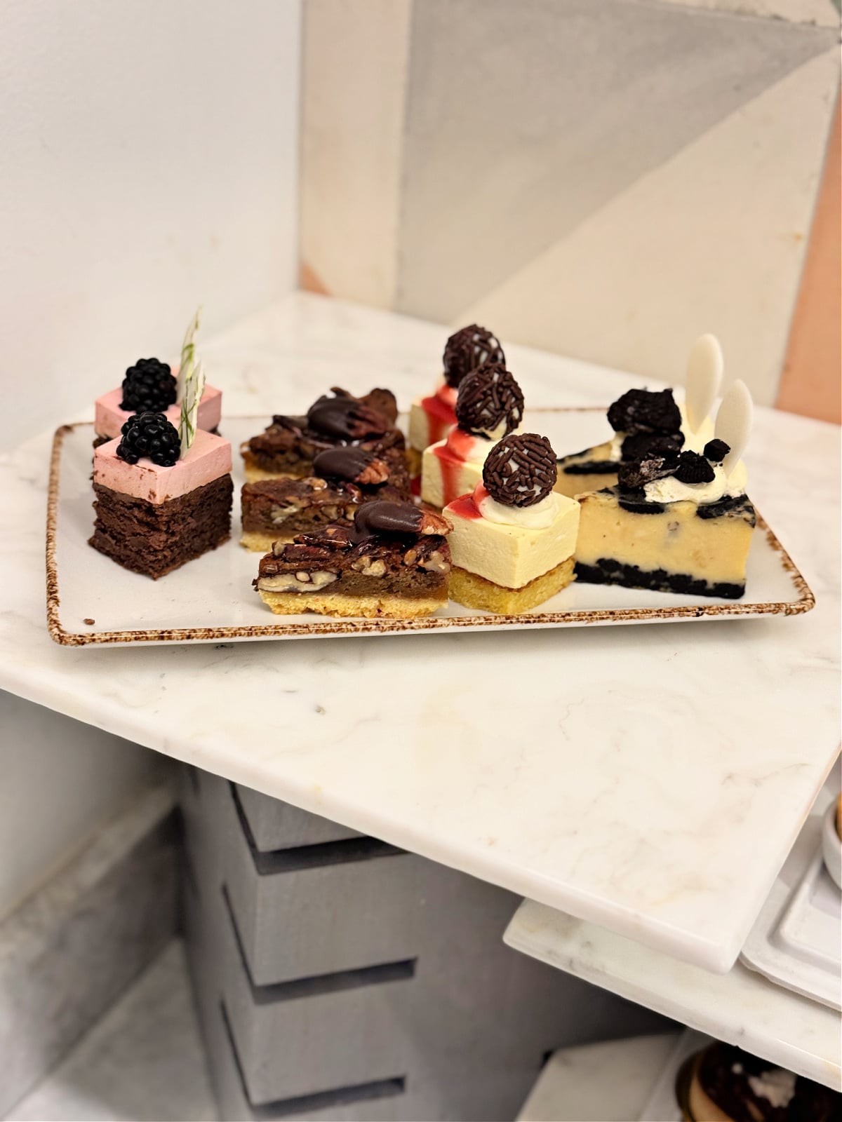 Assorted mini desserts including brownies, cheesecake, and mousse squares arranged on a marble counter.