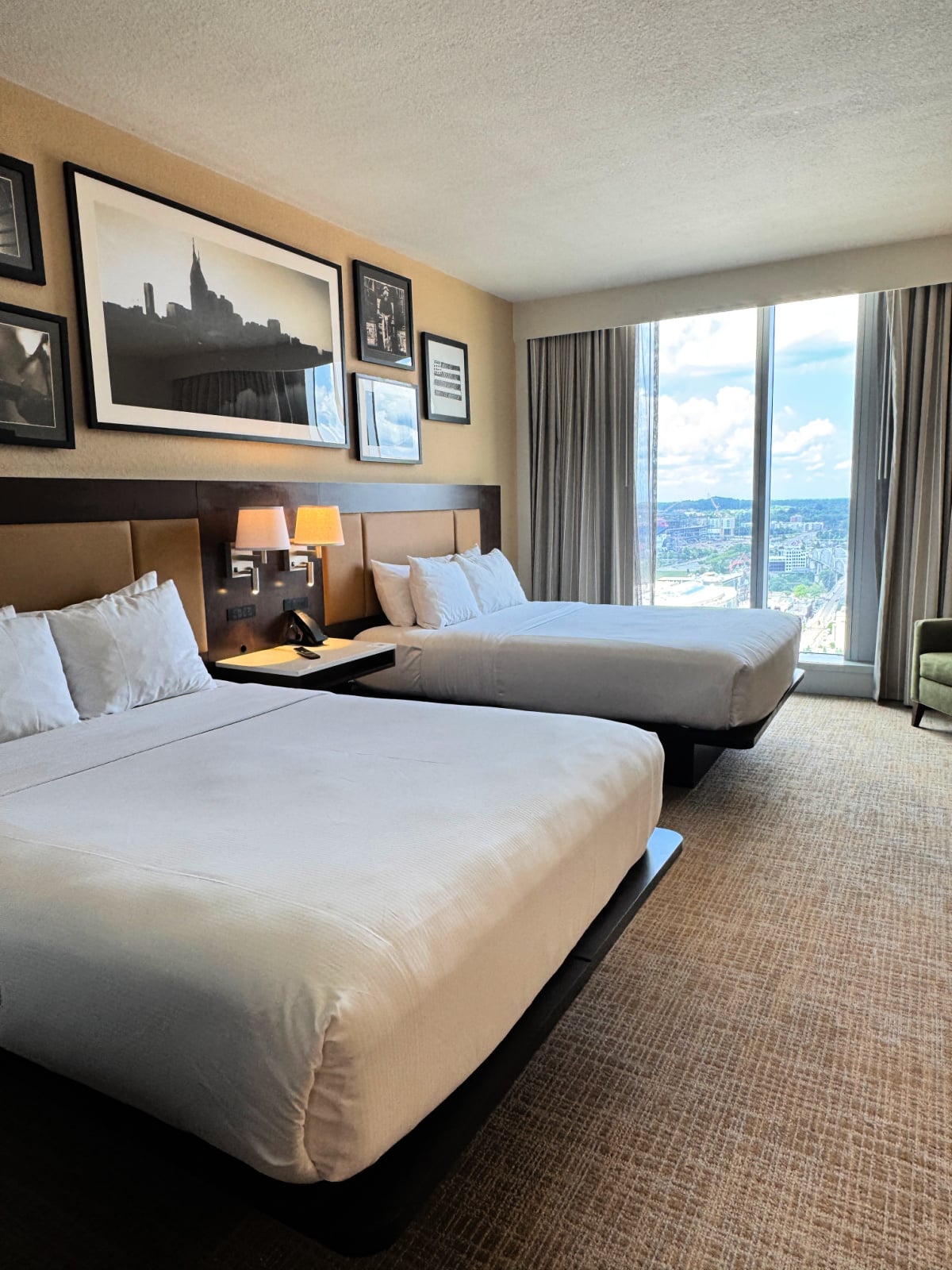 Two queen beds inside a modern Embassy Suites hotel room in downtown Nashville with floor-to-ceiling city views.