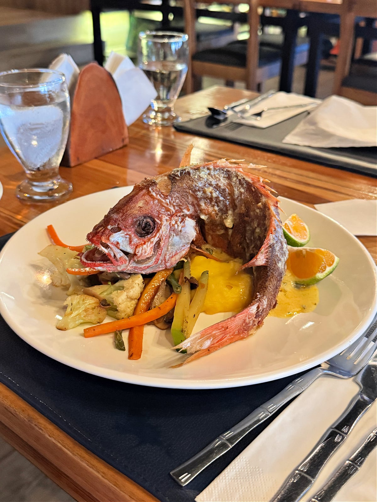 Whole fried red snapper served with sautéed vegetables and citrus slices at a restaurant in Costa Rica.
