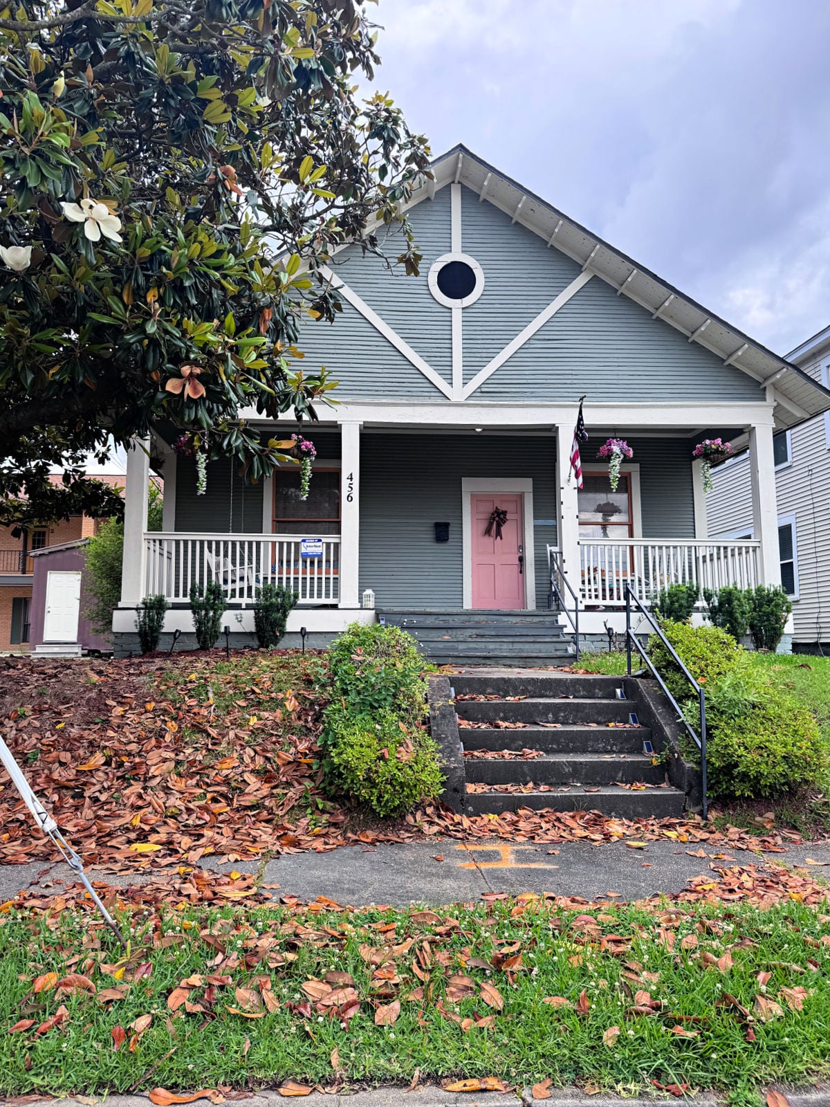 Charming gray cottage in Laurel featuring a pink front door, white porch railing, and hanging flower baskets.