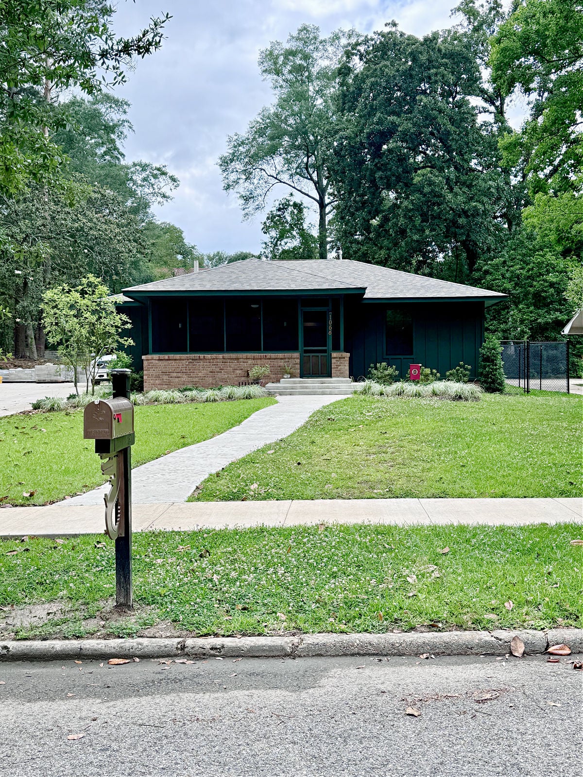 Dark green bungalow-style home with brick accents, a curved walkway, and a neatly maintained front lawn.