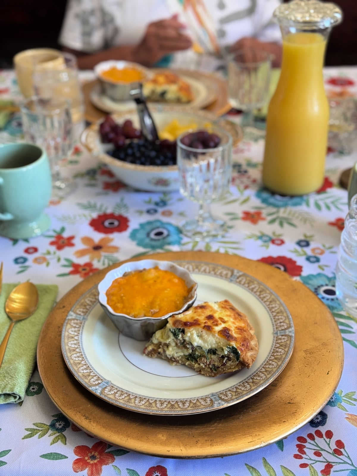 Plated Southern breakfast with quiche and baked dish, served on fine china with fresh fruit and orange juice on a floral tablecloth.