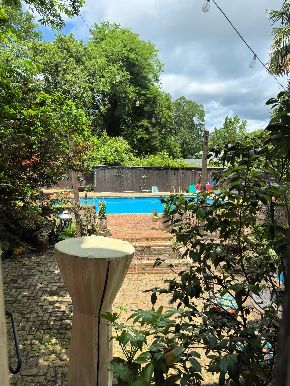Brick courtyard with string lights and a private backyard swimming pool surrounded by lush greenery.