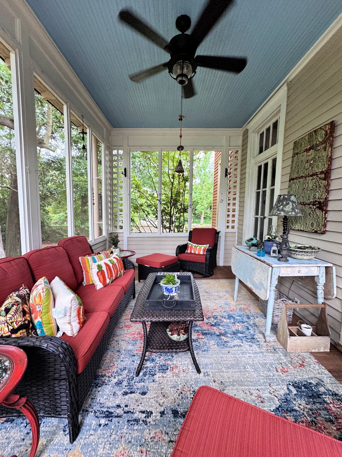 Screened-in porch with wicker furniture, red cushions, ceiling fan, and decorative accents at Jenny’s 1905 Bed & Breakfast.