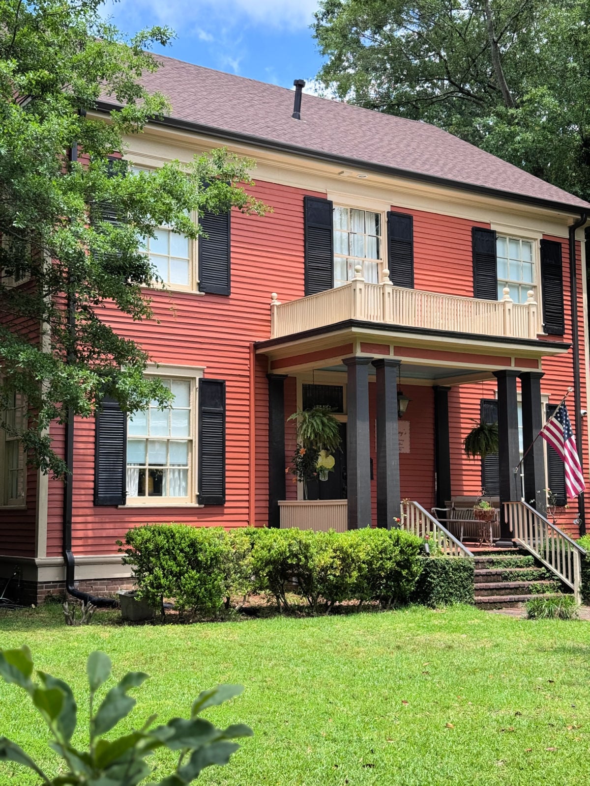 Large historic red home with black shutters, columned front porch, and American flag in Laurel, Mississippi.