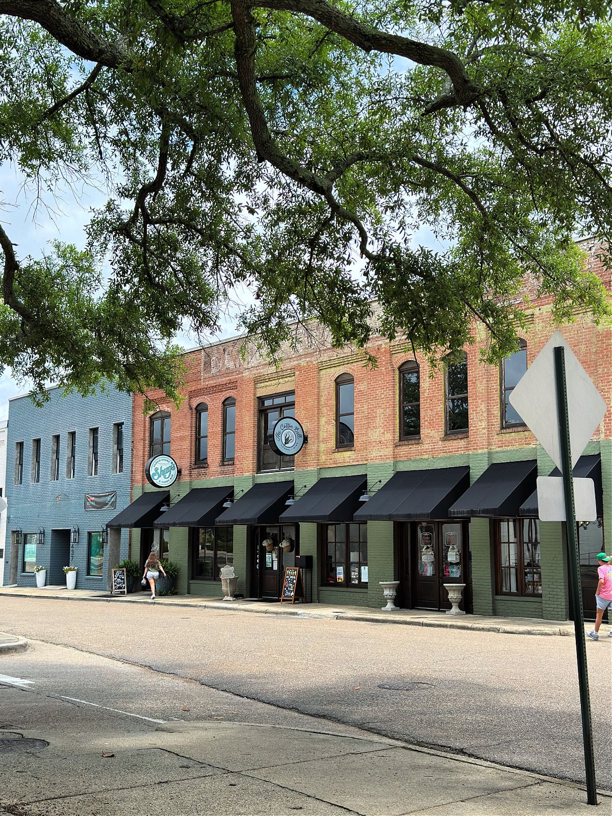 Row of colorful brick storefronts with black awnings along a shaded street in downtown Laurel, Mississippi.