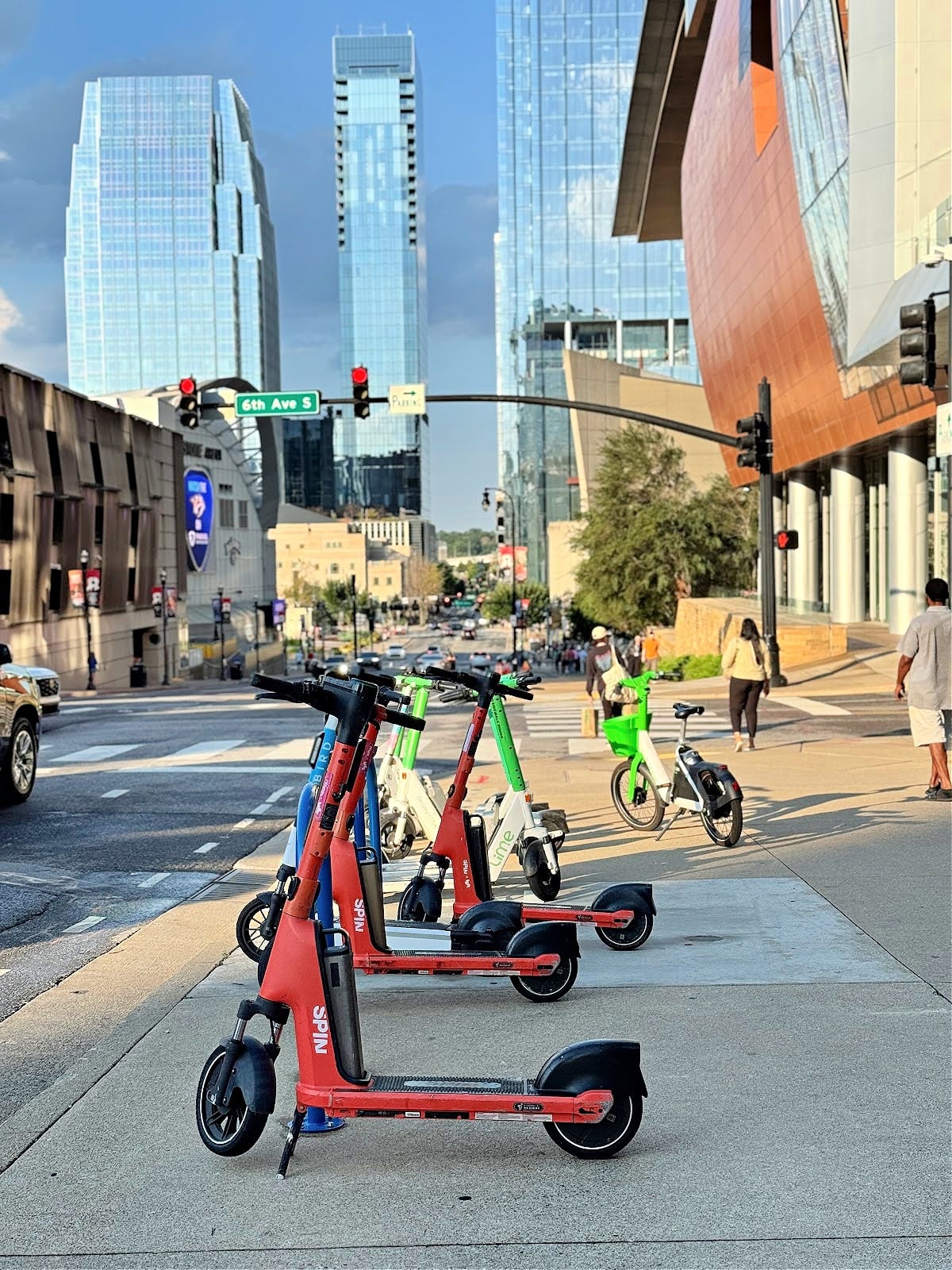 Colorful rental scooters lined up on a sidewalk in downtown Nashville with modern skyscrapers in the background.