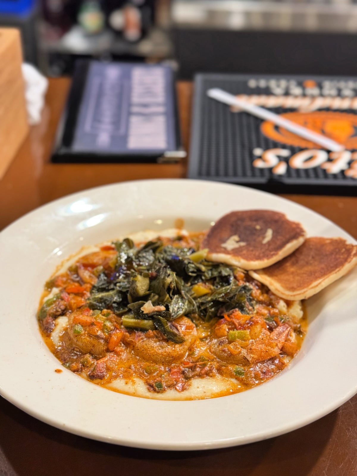 Plate of shrimp and creamy grits topped with sautéed greens and served with cornbread at a Nashville restaurant.