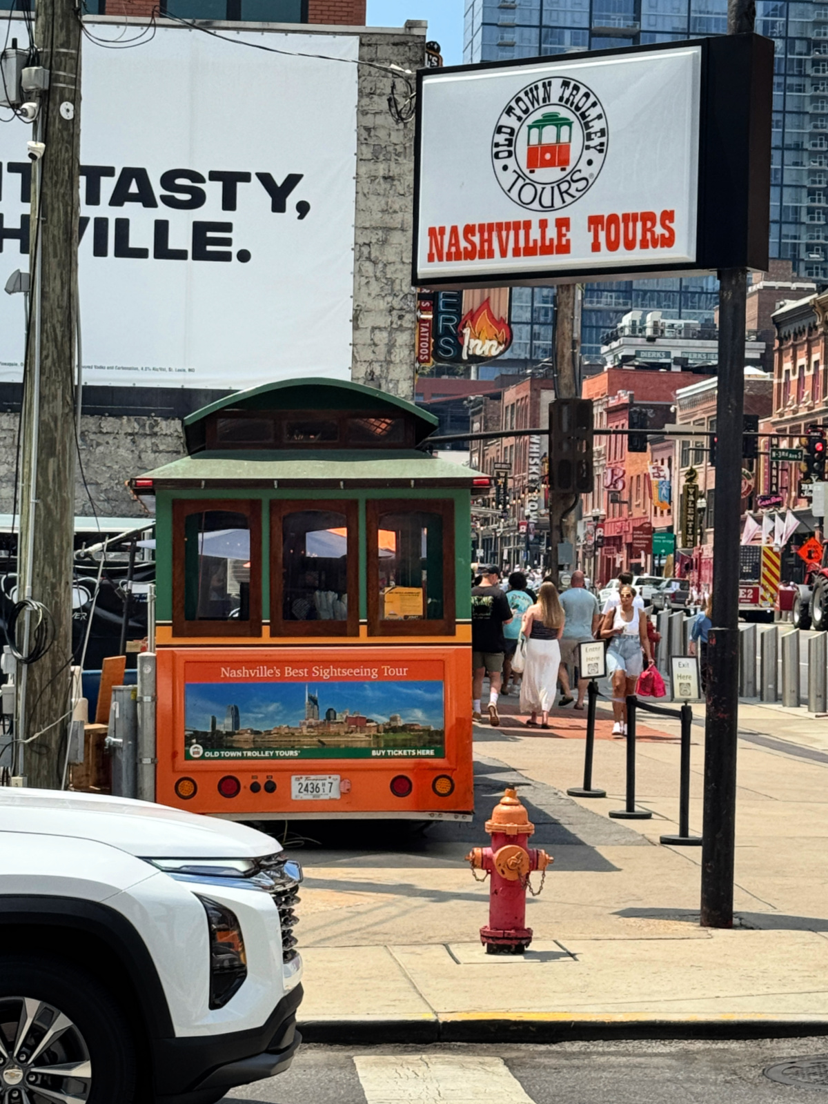 Old Town Trolley Tours vehicle parked on Broadway in downtown Nashville with Nashville Tours sign overhead.