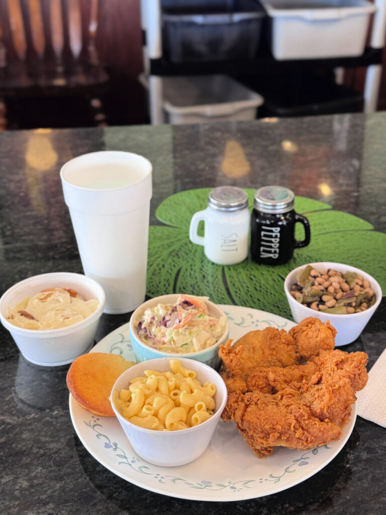 Southern lunch plate with fried chicken, mac and cheese, coleslaw, cornbread, and black-eyed peas on a cafeteria tray.